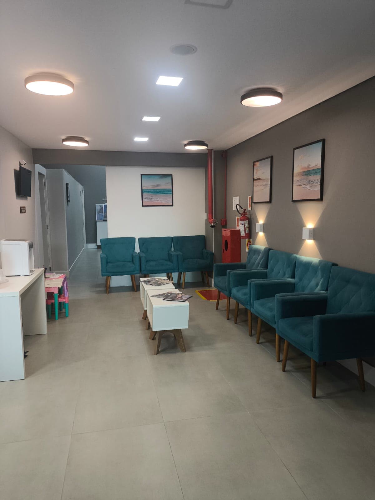 Sala de espera com poltronas verde-petróleo e mesas de centro